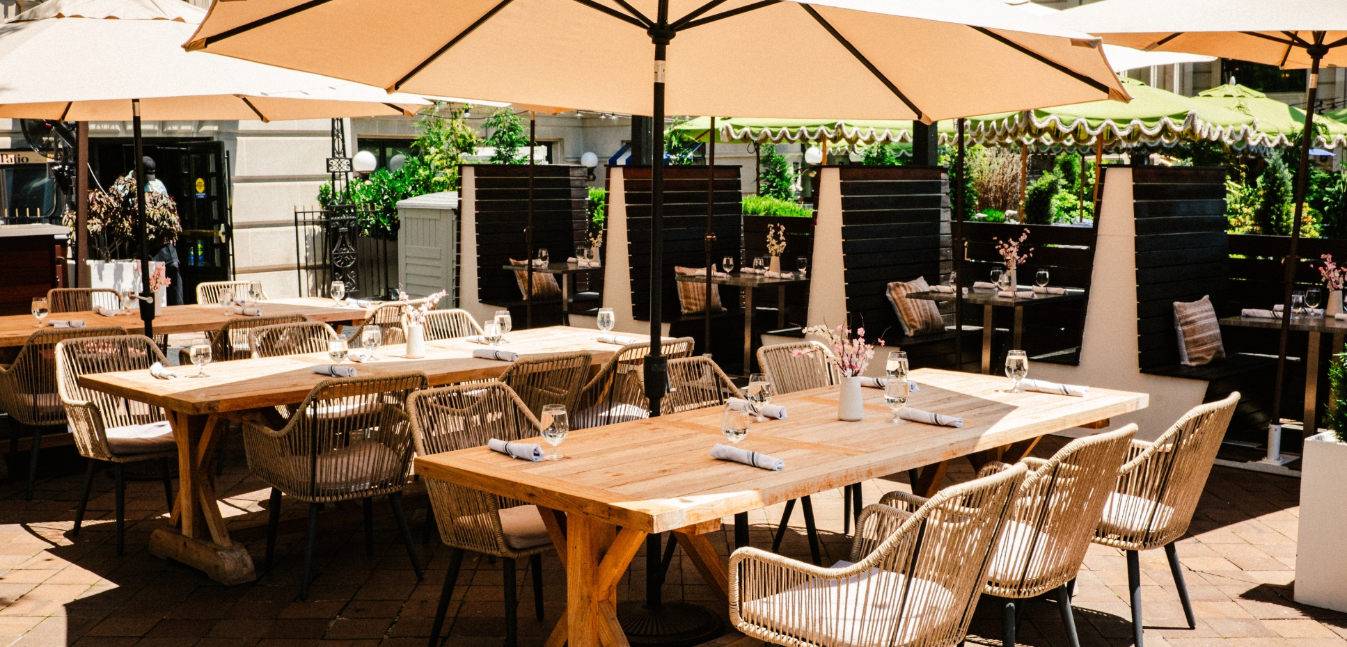 three large light wood tables with several chairs and uoverhead umbrellas