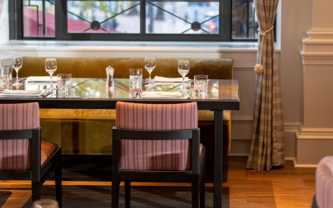 dining table set for four people in front of large window with curtains pulled to left side