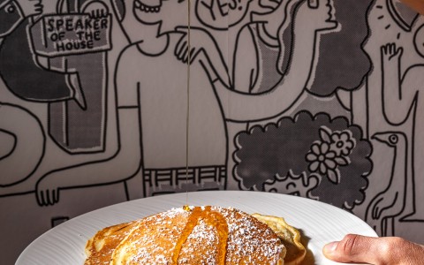 a person pouring syrup onto a plate of pancakes