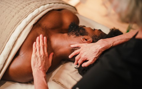 a man lying on a bed with a hand on the neck