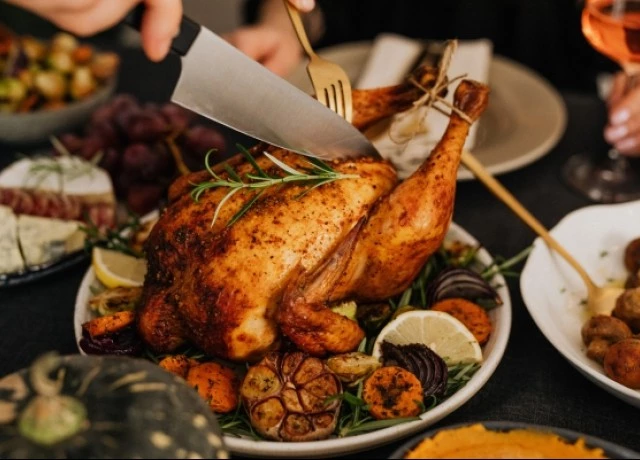 a person cutting a cooked turkey on a plate with a fork and large knife