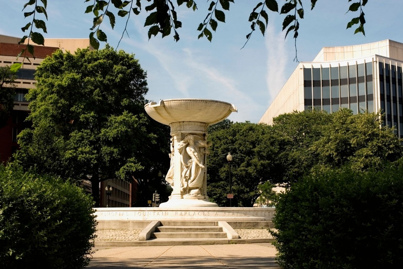 a white fountain with a statue in front of trees