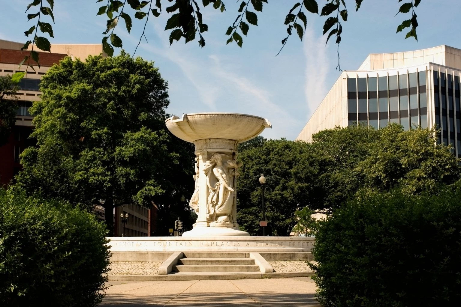 a white fountain with a statue in front of trees