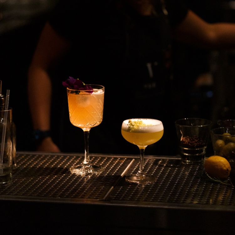 two cocktails on dark bar top