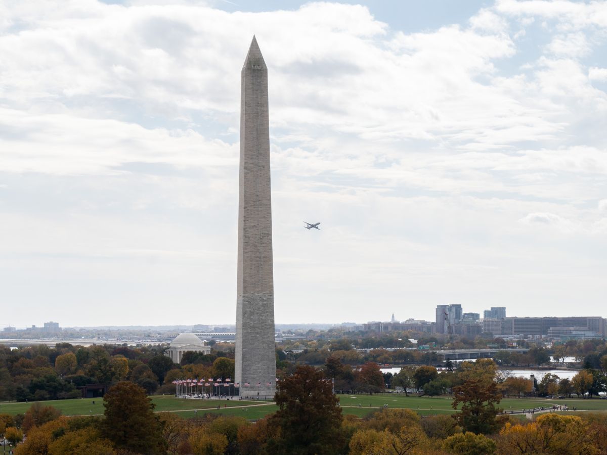 a large monument with a plane flying in the sky with Washington Monument in the background