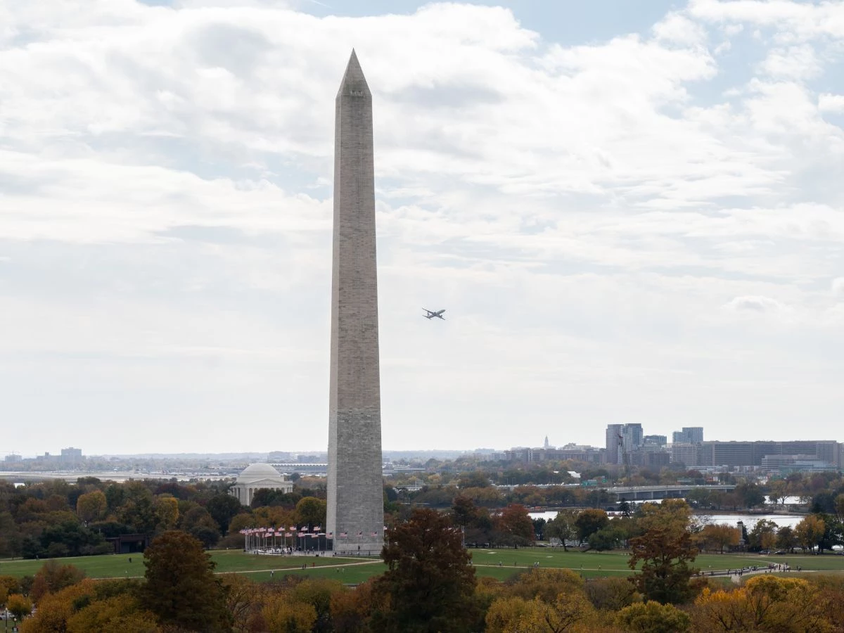 a large monument with a plane flying in the sky with Washington Monument in the background
