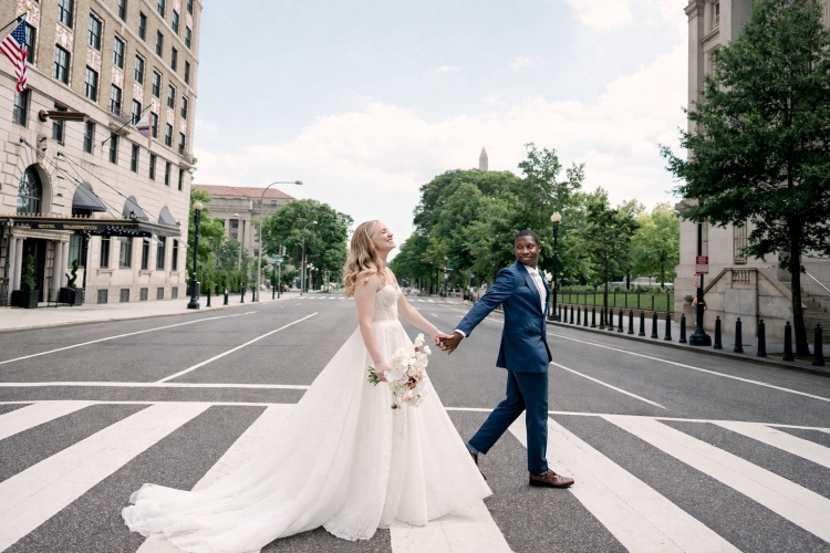 Bride and groom walking across a perfect crosswalk near Hotel Washington with Washington Monument in the background, showcasing iconic wedding venues in Washington DC