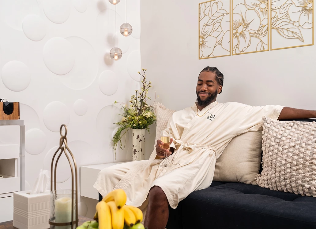 a man in a robe sitting on a couch holding a glass of wine