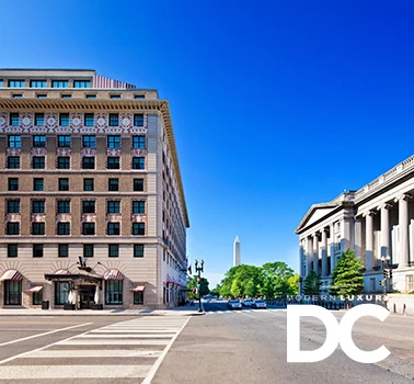 a street with buildings and the washington monument and the modern luxury dc logo