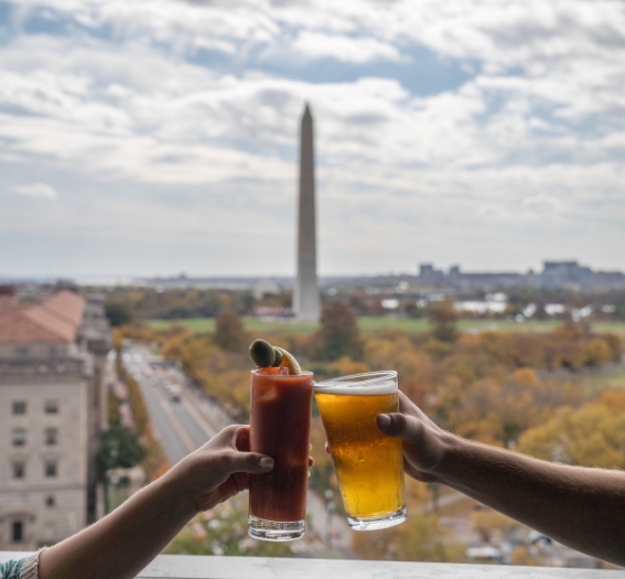 a couple of hands holding drinks in front of a monument