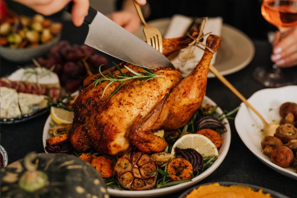 a person cutting a cooked turkey on a plate with a fork and large knife