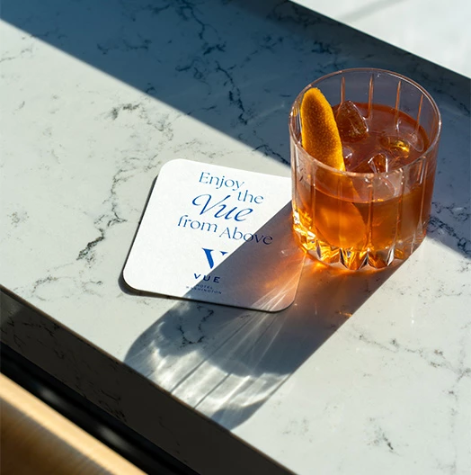 a glass of liquid and a coaster on a counter