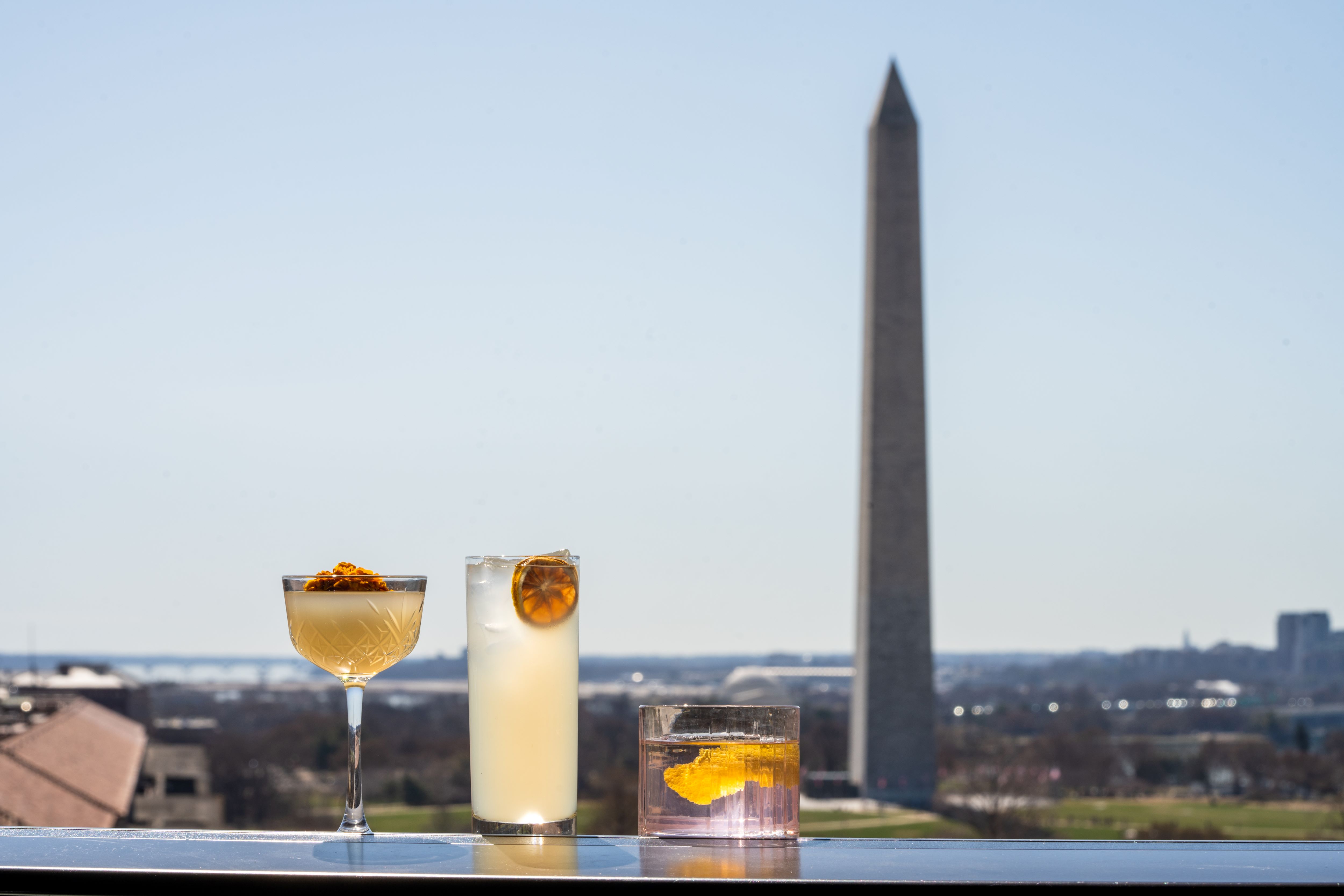 three different cocktails placed on a table with the washington monument in the background