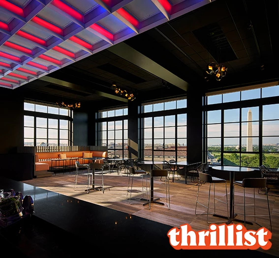 a room with tables and chairs and a large window and the thrillist logo