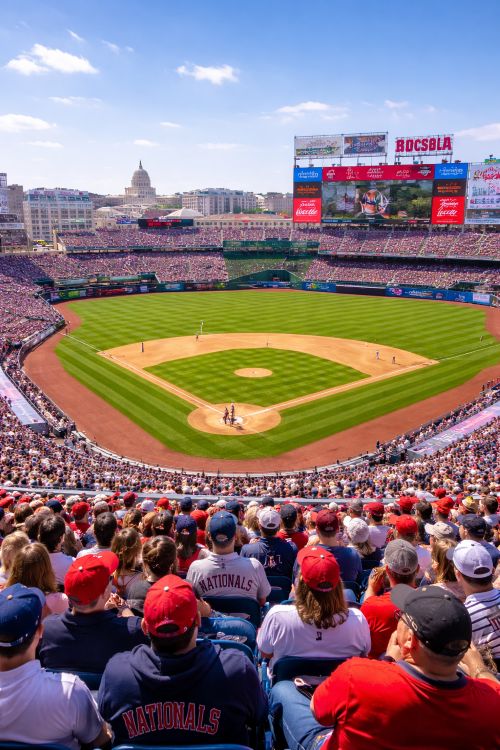 Fans watching a Washington DC baseball game at Nationals Park in March with the Capitol dome visible in the background under clear spring skies