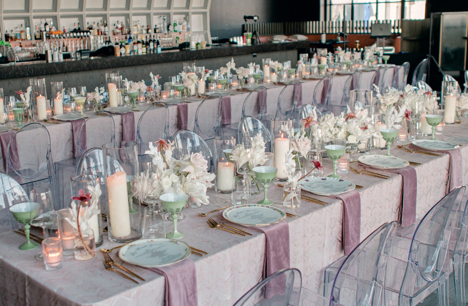two long tables covered in pink tablecloths and set for large group with candles and glassware