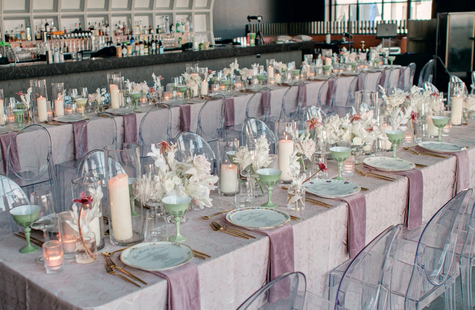 two long tables covered in pink tablecloths and set for large group with candles and glassware