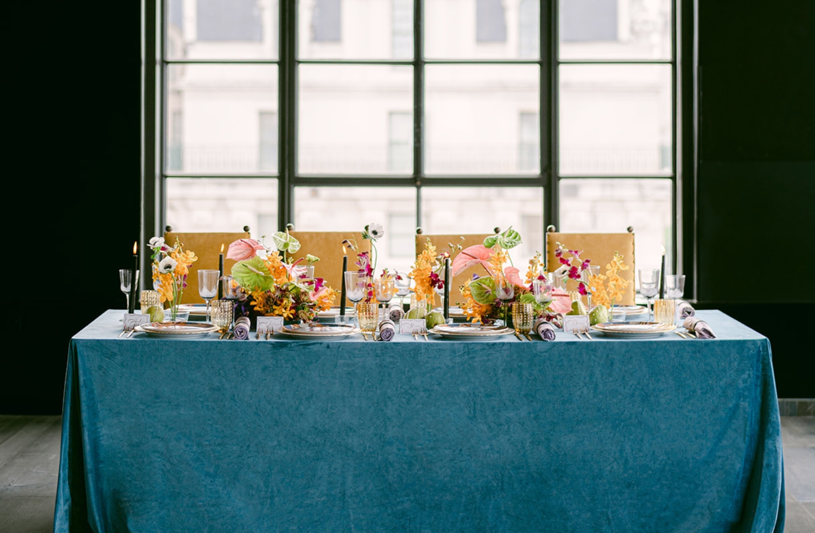 a table covered in blue tablecloth and set for four people with with flowers and plates