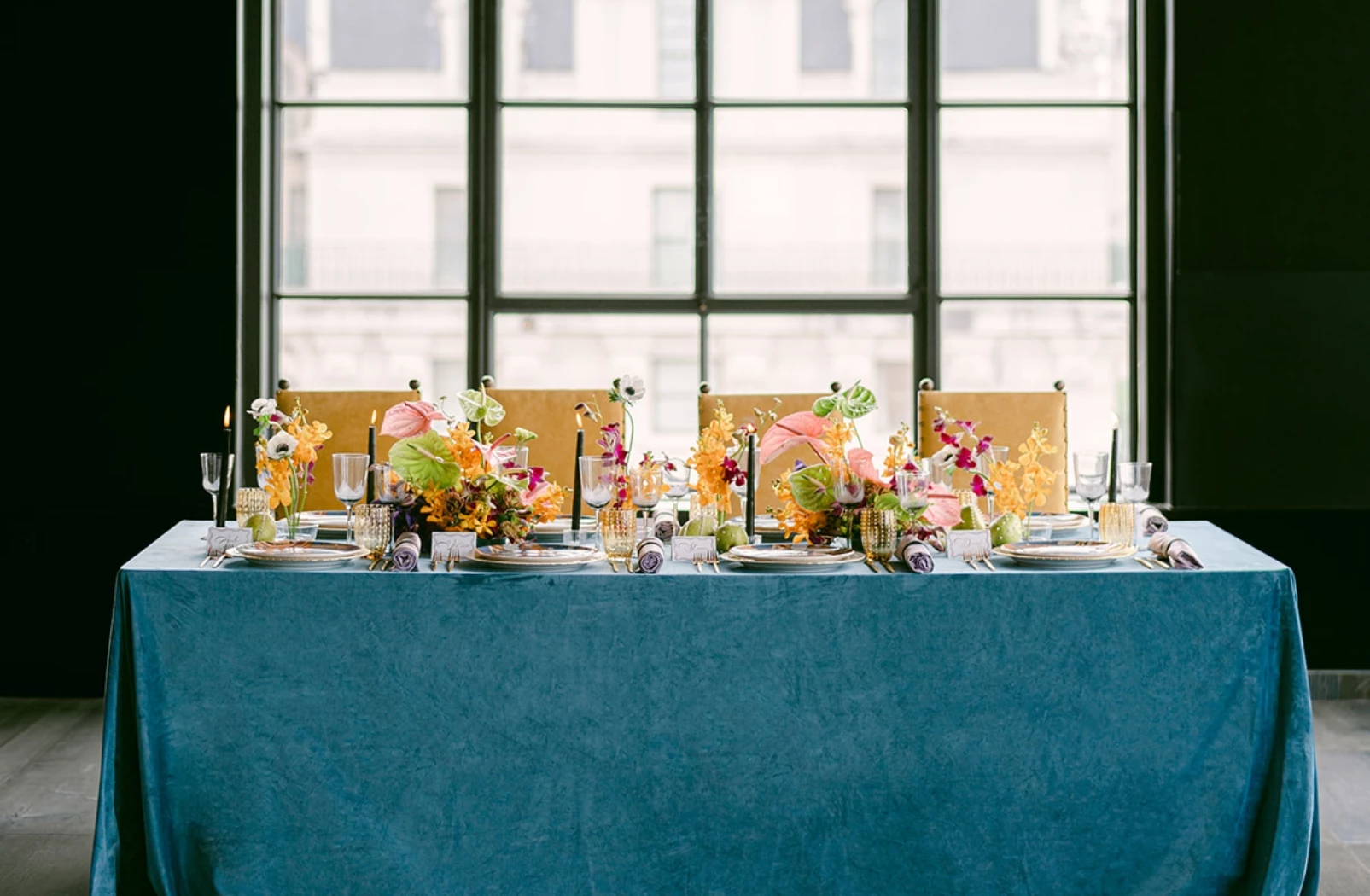 a table covered in blue tablecloth and set for four people with with flowers and plates