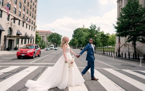 a man and woman in a wedding dress holding hands and walking on a crosswalk