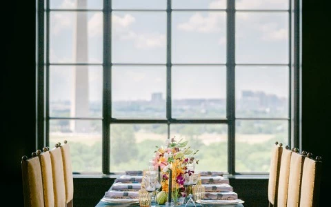 a table with a blue tablecloth and flowers in front of a large window