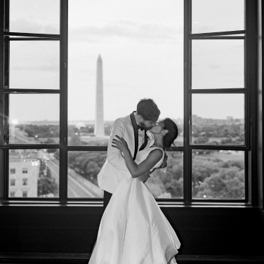 a man and woman kissing in front of a large window with a view of the washington monument