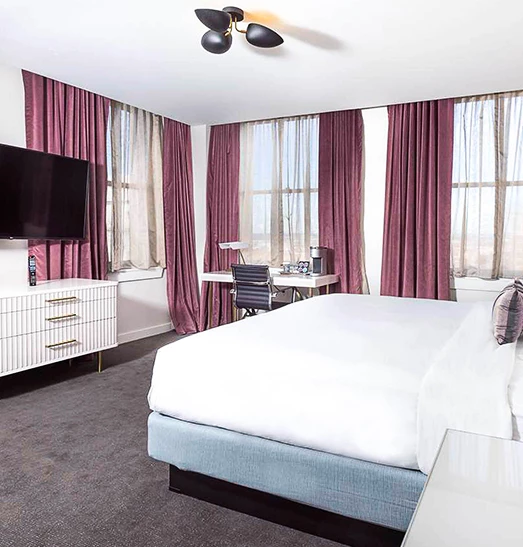 king bed with a tv in front of the bed and violet drapes over the window