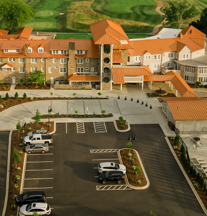 a parking lot with cars and a building with a golf course in the background