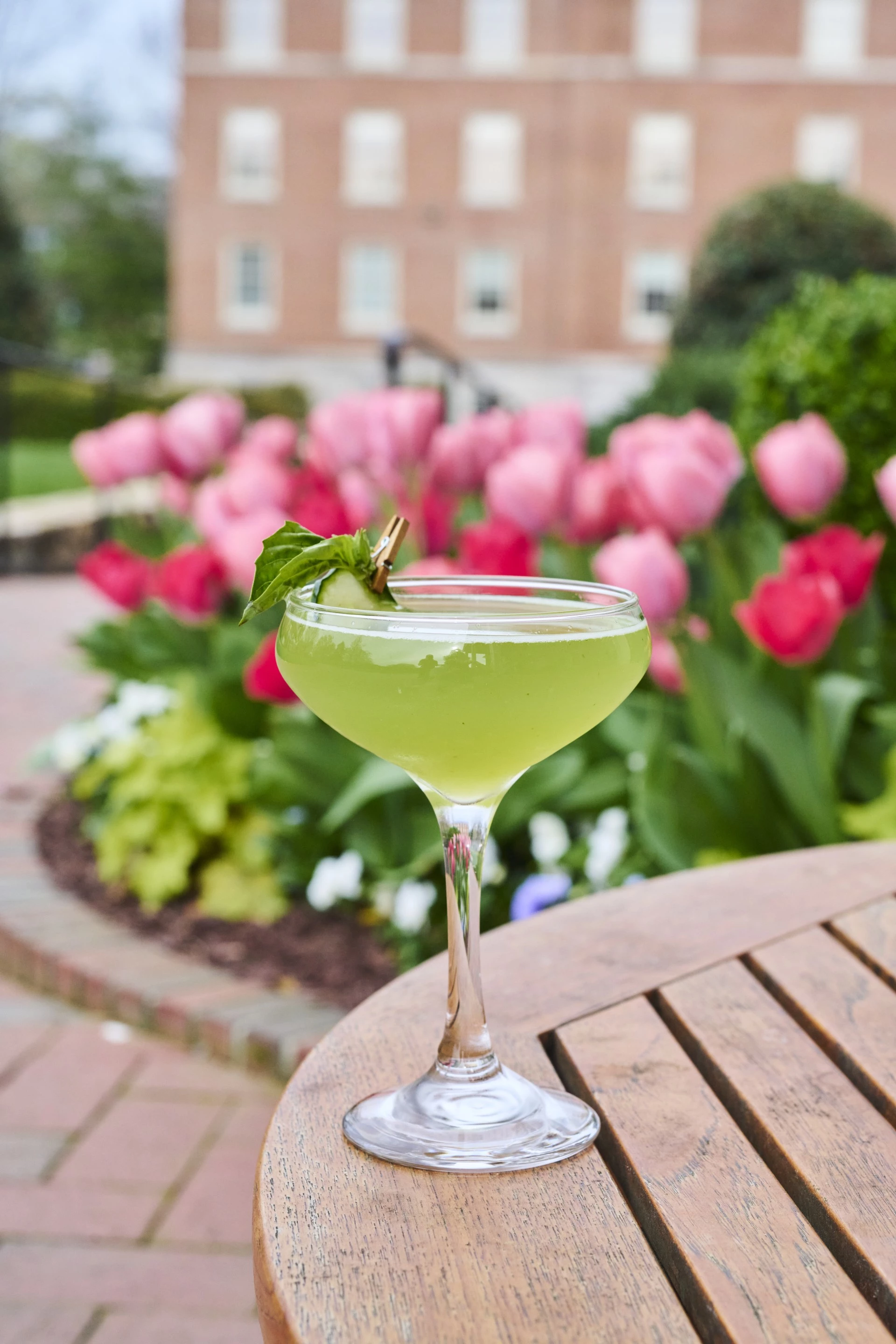 a glass of green liquid on a table with pink flowers in the background