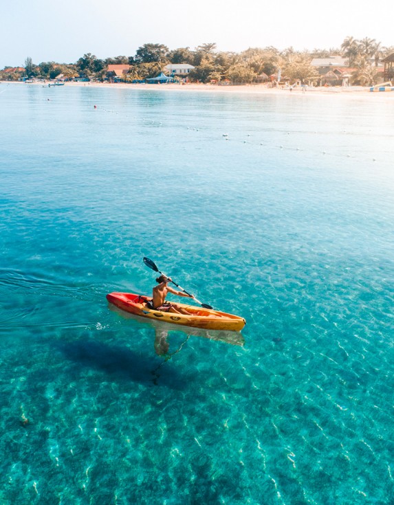A man kayaking in the clear blue water with the sun shining brightly.