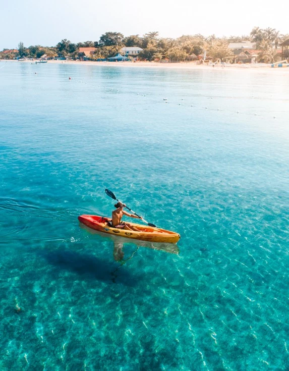 A man kayaking in the clear blue water with the sun shining brightly.