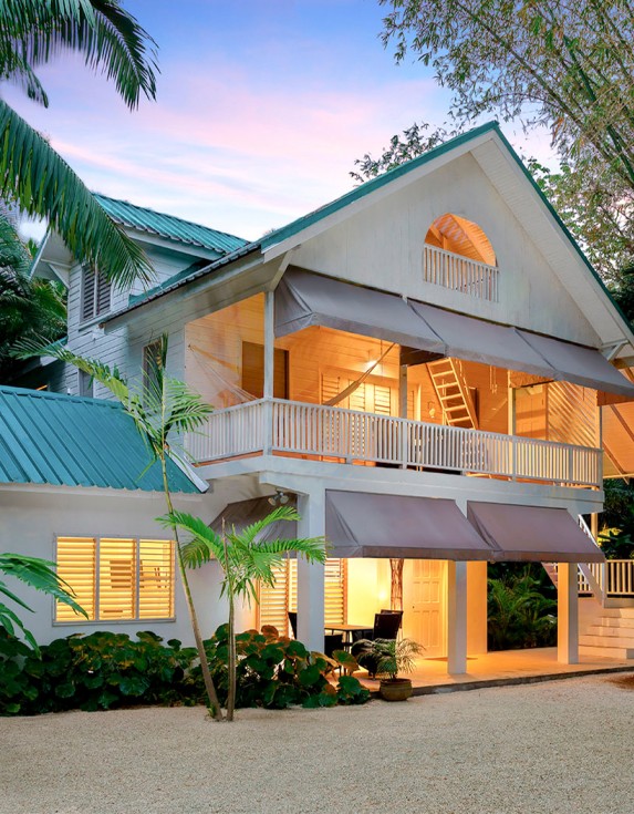 Two story villa at sunset with tropical trees.