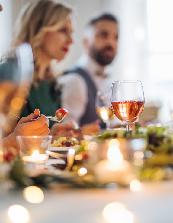 Guests enjoying dinner and glasses of red wine and rose with soft candlelight on the table.