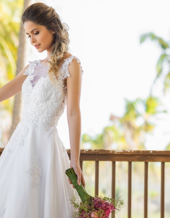Bride wearing a white wedding dress holding a bouquet of flowers looking down at the floor.