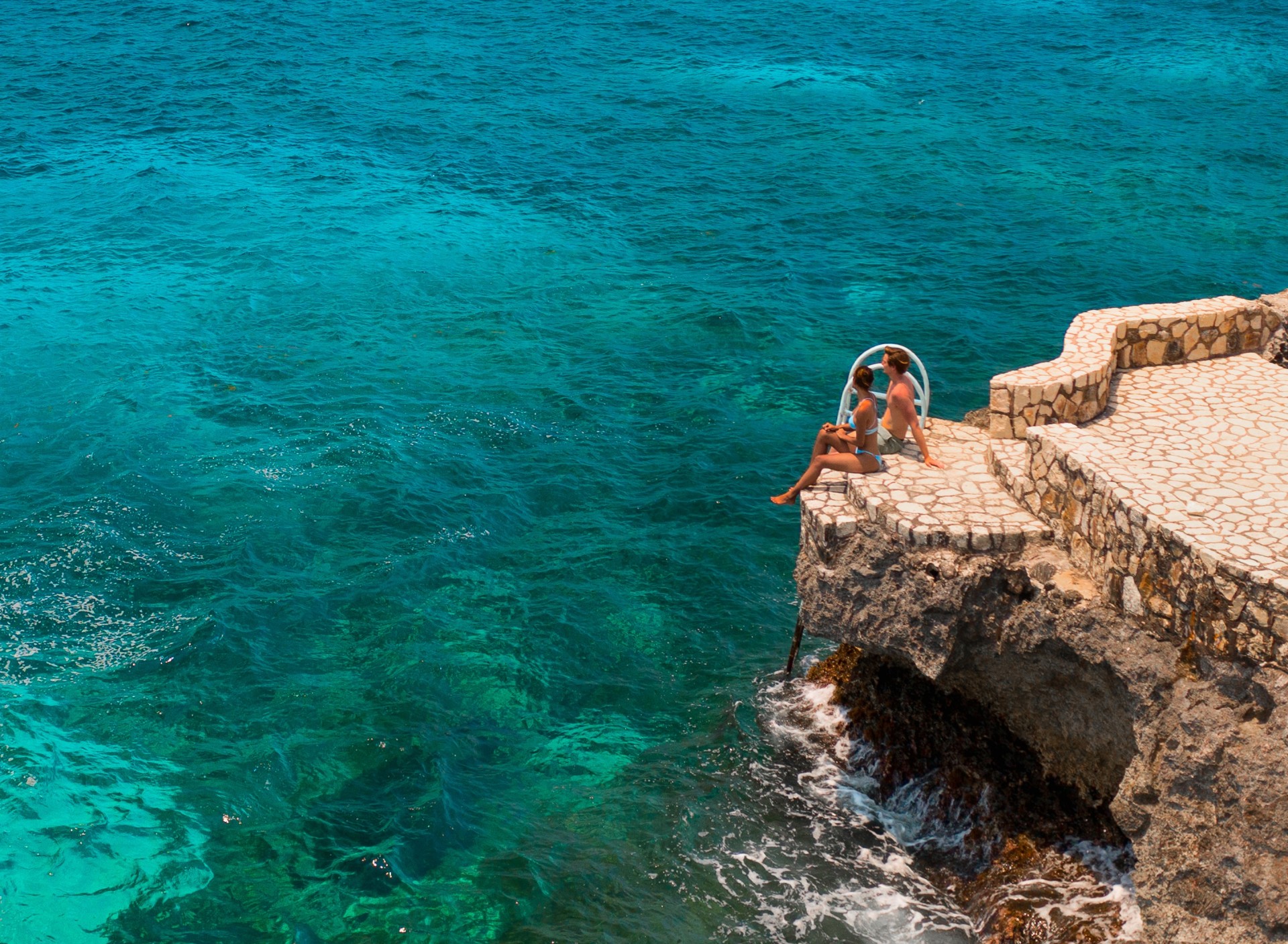 people sitting on a rock ledge overlooking the ocean