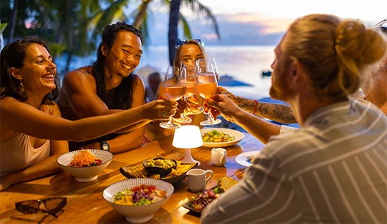 a group of people clinking glasses at a table with food and drinks