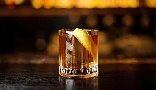 Clear brown cocktail in a rocks glass garnished with a lemon peel.