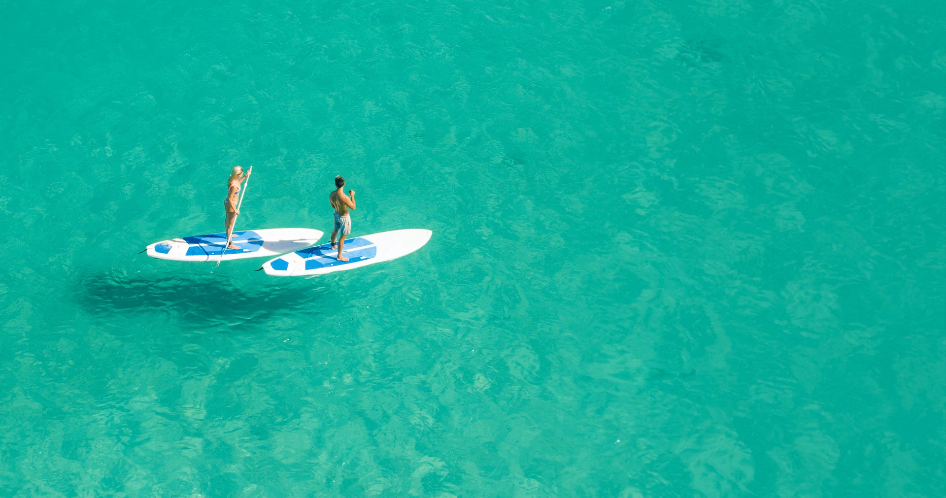 A man and woman stand up paddle boarding in the clear ocean water.