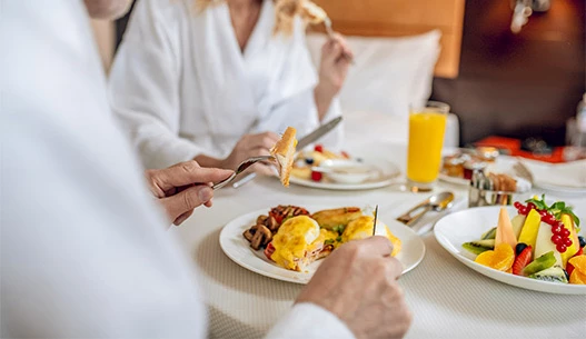 Male and female enjoying eggs benedict and fresh fruit with a glass of fresh squeezed orange juice.