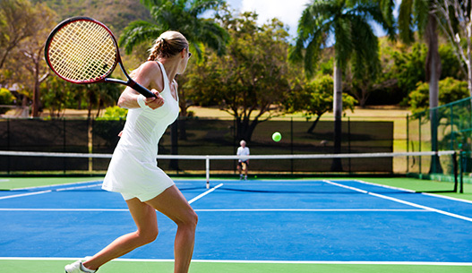 Woman wearing a white tennis tank and skirt getting ready to hit tennis ball to the other side of the court.
