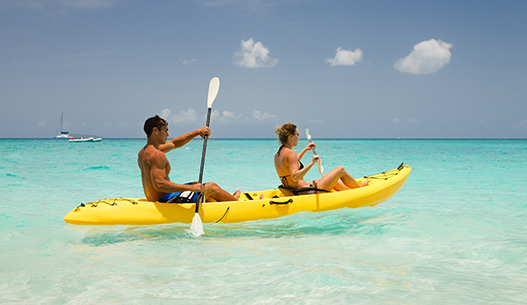 Male and female in a yellow kayak in the clear blue water with the sun shining.