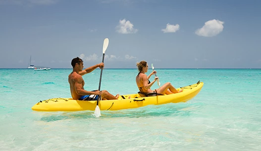 Male and female in a yellow kayak in the clear blue water with the sun shining.