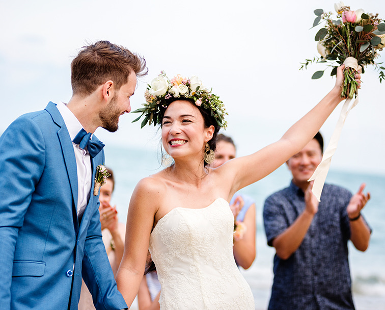 A bride and a groom smiling at each other while guests are clapping.