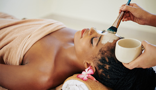 Female laying down with her head propped on rolled towels getting a mask painted on her face during a spa service.