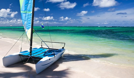 A white and blue sailboat beached on the sand during the day with the sun shining brightly.