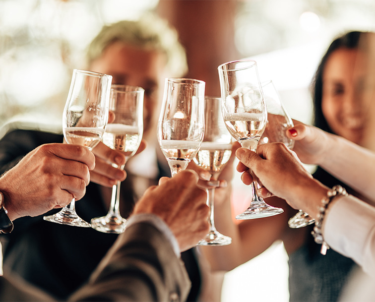 A group of friends clinking stemmed glasses with clear liquid in it.