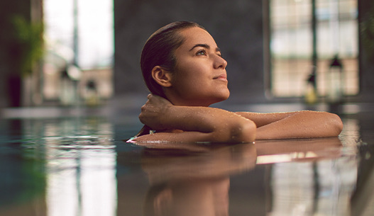 A woman in the water looking up at the dim light coming in from above.