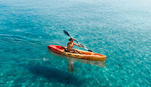 A male kayaking in the blue water with the sun shining.