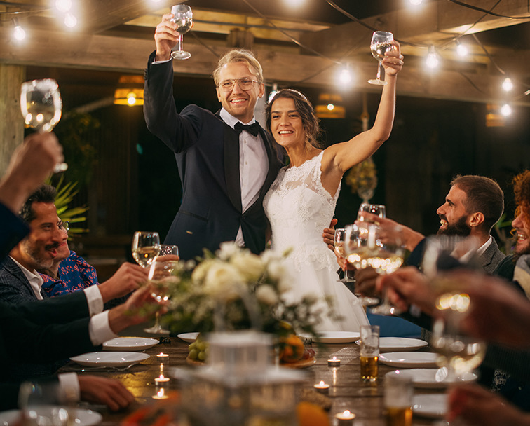Smiling bride and groom giving a toast to the guests with soft lighting overhead.