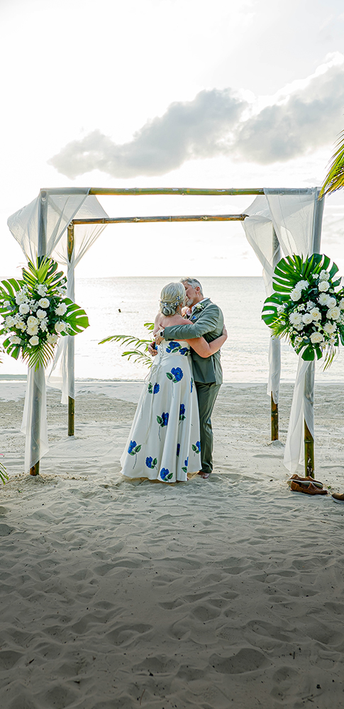 a man and woman kissing under a wedding arch on a beach